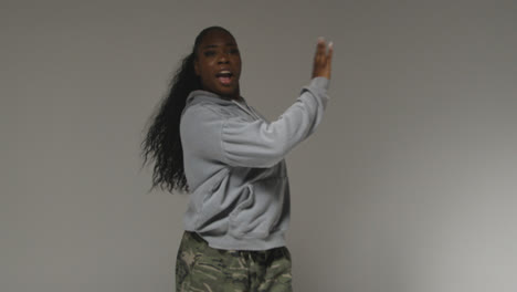 Studio-Portrait-Shot-Of-Young-Woman-Wearing-Hoodie-Dancing-With-Low-Key-Lighting-Against-Grey-Background-2